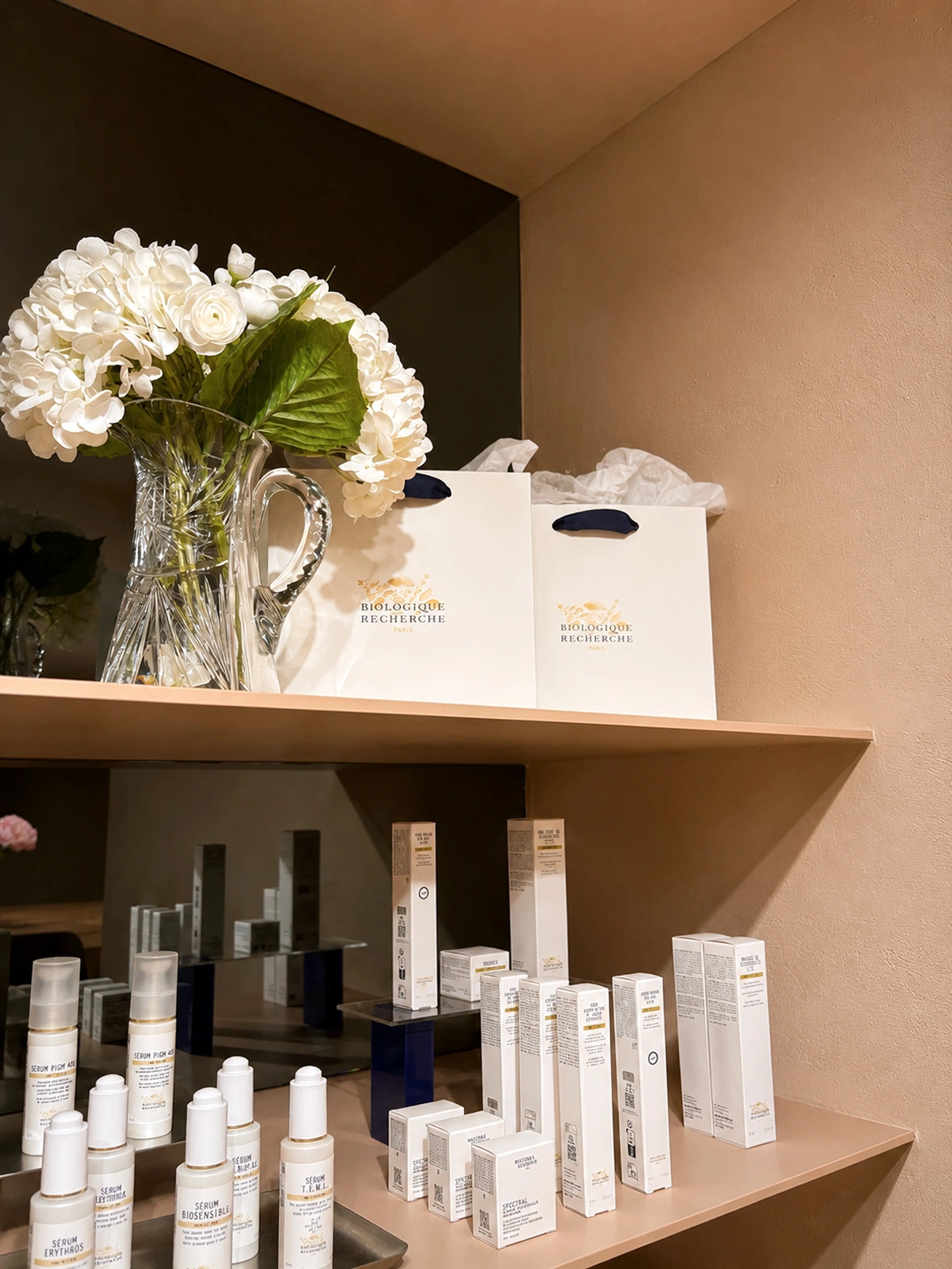 Biologique Recherche skincare and white hydrangeas on a mirrored boutique shelf at Zohar